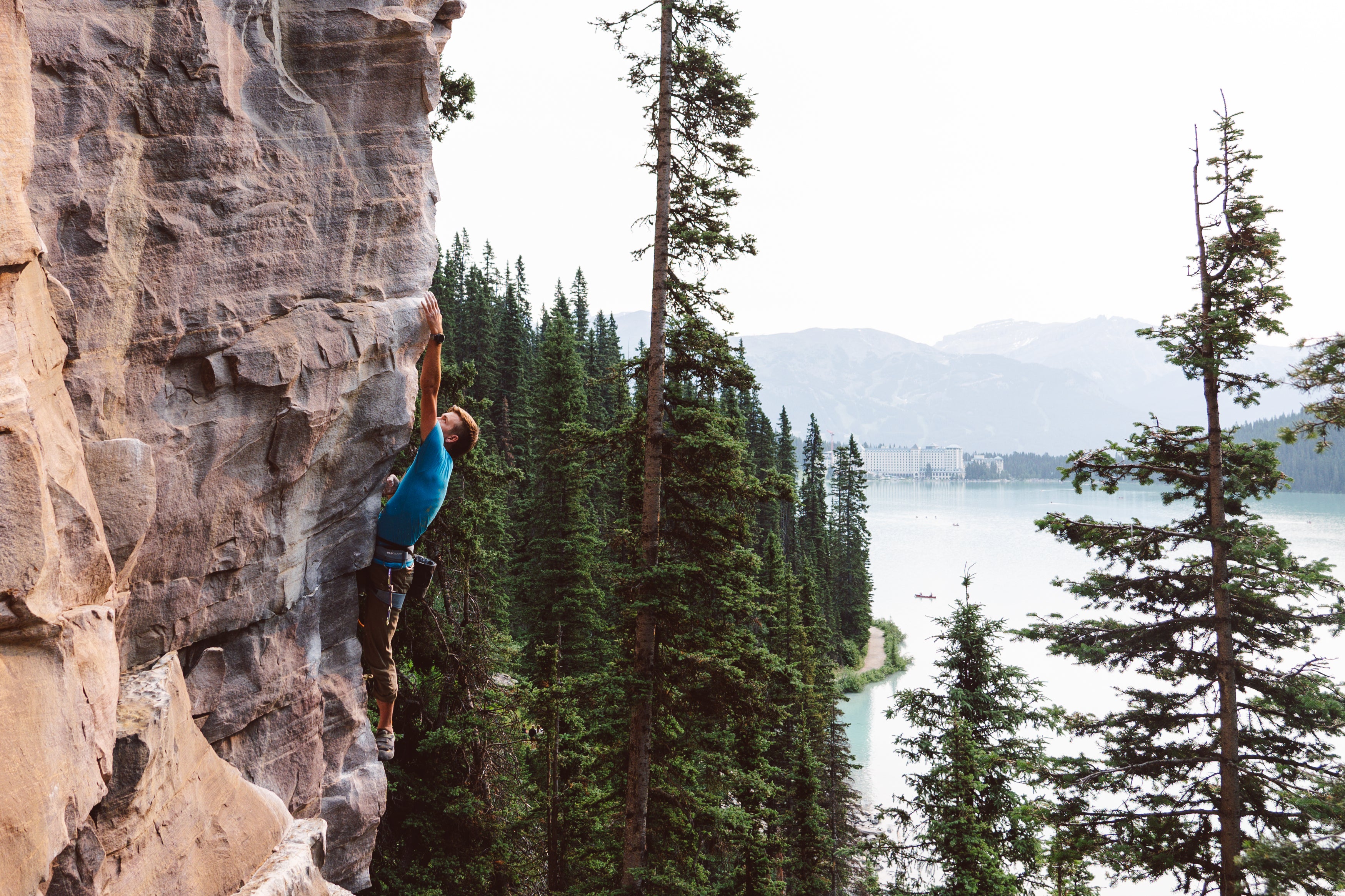 male rock climber in pine trees above a lake